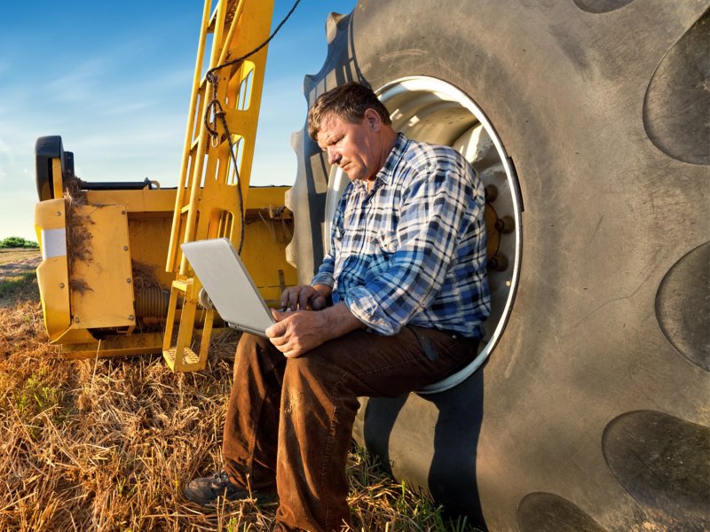 Farmer on laptop sat on tractor wheel